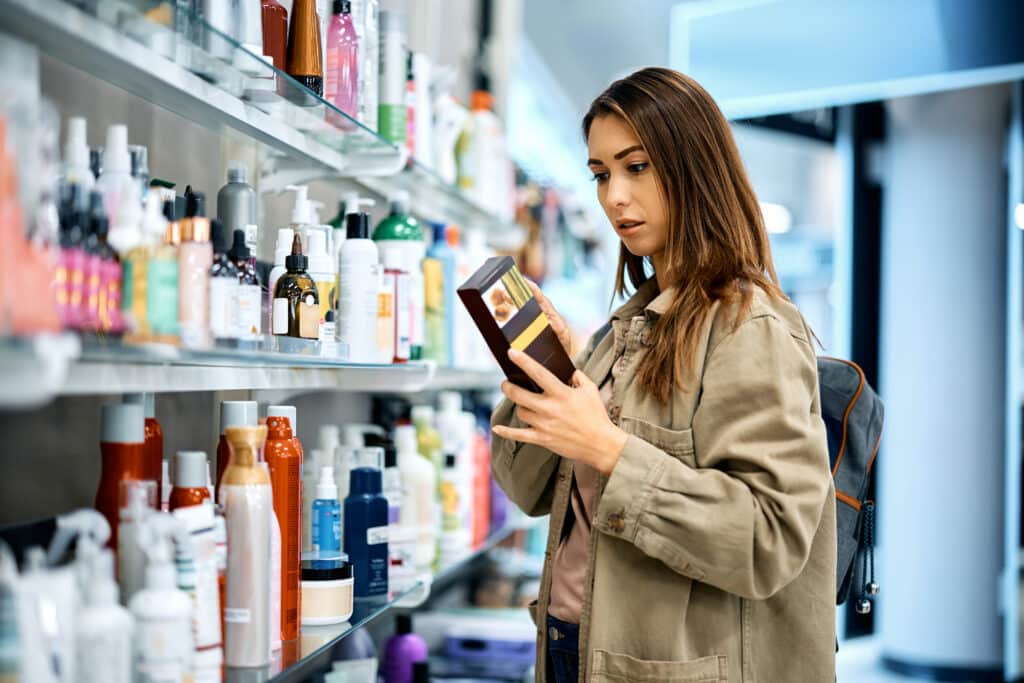 Young woman reading label on skin care product while shopping at the mall.