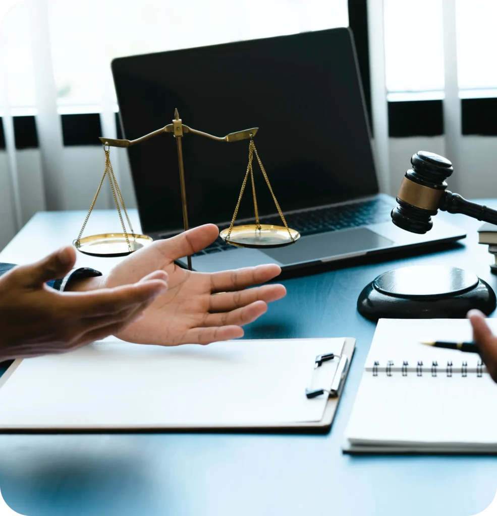 Legal consultation scene with scales of justice, a gavel, a laptop, and documents on a desk, as two people discuss a case